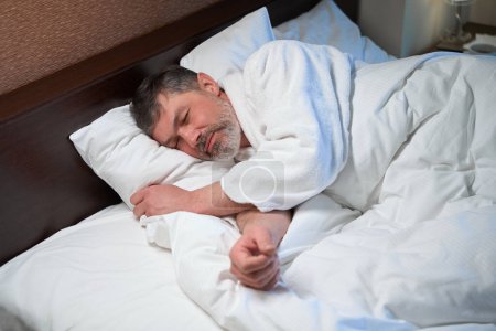 Foto de Varón cansado en albornoz acostado en la cama, durmiendo después del trabajo en la habitación del hotel - Imagen libre de derechos