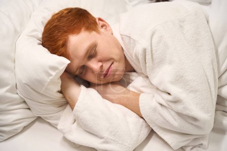 Téléchargez les photos : Un beau roux dort doucement sur un lit d'hôtel doux, un homme loue une chambre confortable - en image libre de droit