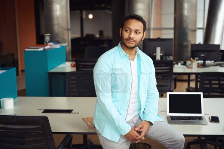 Téléchargez les photos : Jeune homme debout près de la table avec ordinateur portable au travail dans le centre d'affaires - en image libre de droit