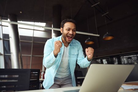 Foto de Hombre de pie cerca del escritorio con el ordenador y se siente feliz en el trabajo en la oficina - Imagen libre de derechos