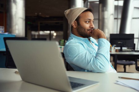 Téléchargez les photos : Jeune homme en coiffure fatigué de travailler sur ordinateur tout en étant assis au bureau dans le centre d'affaires - en image libre de droit