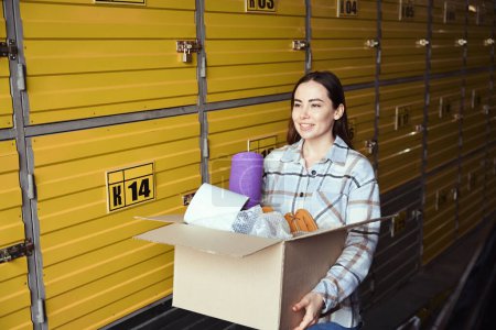 Téléchargez les photos : Femme souriante debout dans l'entrepôt avec une boîte pleine de choses dans ses mains - en image libre de droit