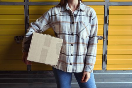 Téléchargez les photos : Photo recadrée d'une femelle debout dans l'entrepôt avec une boîte à la main - en image libre de droit