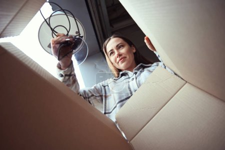 Téléchargez les photos : Vue basse d'une femme satisfaite tenant un objet sur une boîte en carton - en image libre de droit