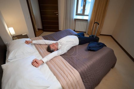 Foto de Hombre feliz en traje de negocios descansando en la cama en el hotel después de viajar - Imagen libre de derechos