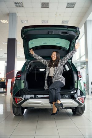 Schöne Asiatin freut sich über ein neues Auto, der Kofferraum ist offen