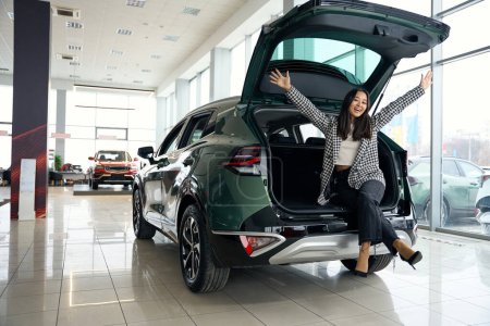 Schöne junge Frau freut sich über neues Auto, der Kofferraum ist offen