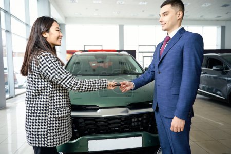 Foto de Mujer asiática toma las llaves del coche de un hombre en un traje de negocios, la gente está de pie cerca de un coche nuevo brillante - Imagen libre de derechos