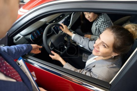 Téléchargez les photos : Deux femmes heureuses en costumes regardant de l'automobile et diriger leur regard vers la personne - en image libre de droit