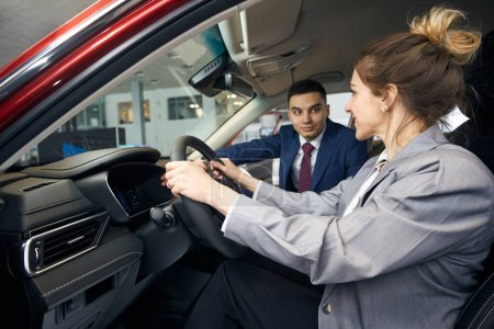 Photo for Man in suit on passenger seat looking at woman in jacket holding steering wheel - Royalty Free Image