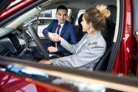 Photo for Smiling businessman and lady in suit shaking hands while sitting on front seats in automobile - Royalty Free Image