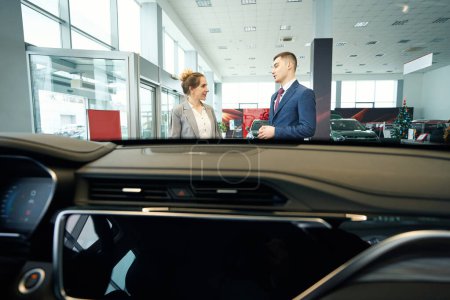 Foto de Feliz hombre y señora en trajes hablando en auto concesionario coche exterior - Imagen libre de derechos
