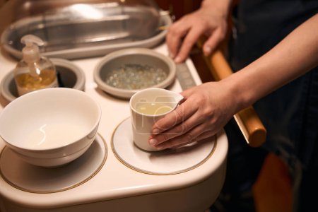 Photo for Cropped photo of masseuse hands touching ceramic bowl filled with medicated oil - Royalty Free Image