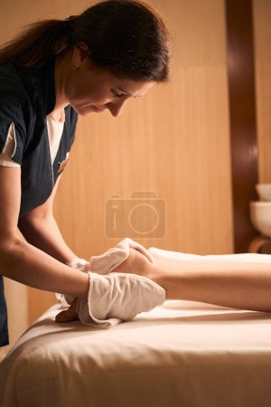 Téléchargez les photos : Vue latérale de masseuse mature essuyant le pied du client féminin avec une serviette propre - en image libre de droit