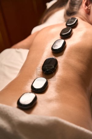 Téléchargez les photos : Photo recadrée d'une femme allongée sur une table de massage avec des pierres de basalte chaudes sur le dos - en image libre de droit