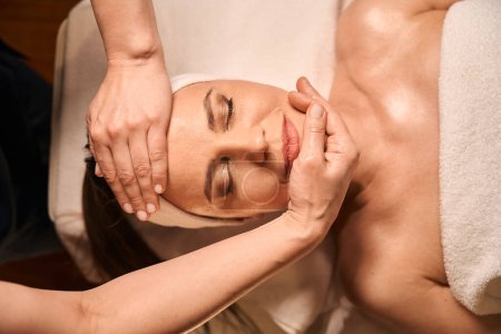 Photo for Massotherapist hands relaxing female client facial muscles during massage session - Royalty Free Image