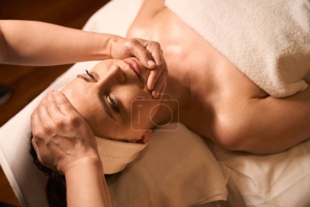 Photo for Wellness center massotherapist placing hands on chin and forehead of tranquil mature lady - Royalty Free Image