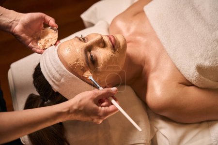 Photo for Spa salon cosmetician applying mask to face of calm adult woman with brush - Royalty Free Image