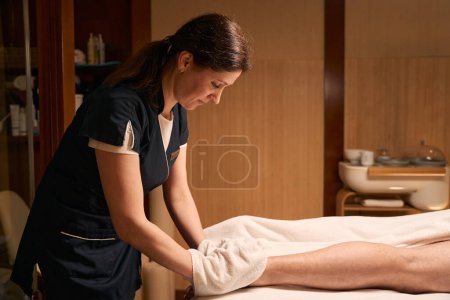 Photo for Focused masseuse removing dead skin cells from male heel with exfoliating mittens - Royalty Free Image