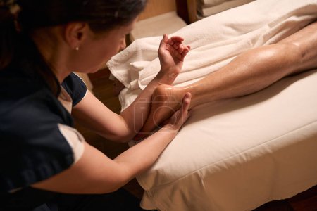 Téléchargez les photos : Photo recadrée d'un thérapeute spa massant le pied d'un homme adulte à l'aide d'un avant-bras - en image libre de droit