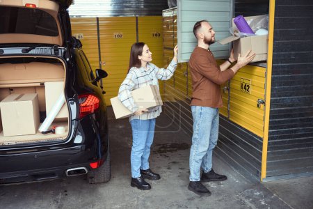 Foto de Un par de personas contentas de pie detrás del coche y apilando cajas de cosas en el casillero - Imagen libre de derechos