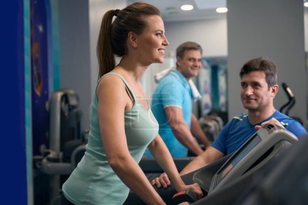 Photo for Smiling fit woman working out on treadmill under supervision of gym trainer - Royalty Free Image