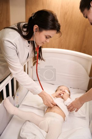 Téléchargez les photos : Médecin pédiatrique sérieux à l'écoute des petits battements de cœur de l'enfant avec stéthoscope avec assistance parentale - en image libre de droit
