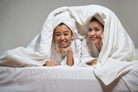 Téléchargez les photos : Photo de deux copines sous une couverture dans un hôtel. Femme se cacher sous couverture sur le lit dans la chambre d'hôtel - en image libre de droit