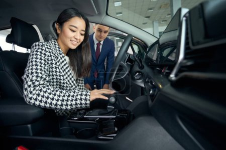 Téléchargez les photos : Acheteur est heureux d'inspecter l'intérieur de la voiture avant d'acheter, à côté du gestionnaire est un consultant - en image libre de droit