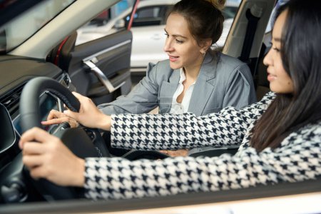 Téléchargez les photos : Deux femmes d'affaires joyeux regardent le tableau de bord de la voiture tandis que et assis dans l'automobile - en image libre de droit