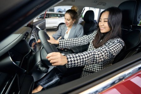 Téléchargez les photos : Deux femmes d'affaires joyeux regardent le tableau de bord de la voiture tout en étant assis dans l'automobile - en image libre de droit