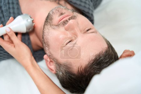 Photo for Middle-aged patient on the procedure of RF lifting in a medical institution, the beautician uses modern equipment - Royalty Free Image