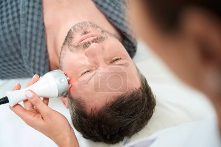 Foto de Hombre de mediana edad en el procedimiento de elevación de RF en la clínica de medicina estética, cosmetólogo utiliza equipos modernos - Imagen libre de derechos