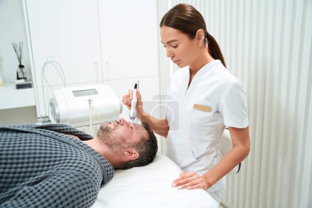 Photo for Female in medical uniform performs an RF lifting procedure on a middle-aged man, a specialist uses a modern apparatus - Royalty Free Image