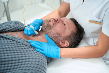 Photo for Middle-aged male on a laser microdermabrasion cosmetic procedure, an esthetician uses an innovative apparatus - Royalty Free Image