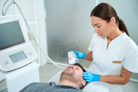 Foto de Hombre de mediana edad en un procedimiento de elevación masiva, un cosmetólogo trabaja con el área frontal de los pacientes - Imagen libre de derechos