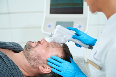 Photo for Middle-aged male on the mass lifting procedure, the cosmetologist works with the patients frontal area - Royalty Free Image