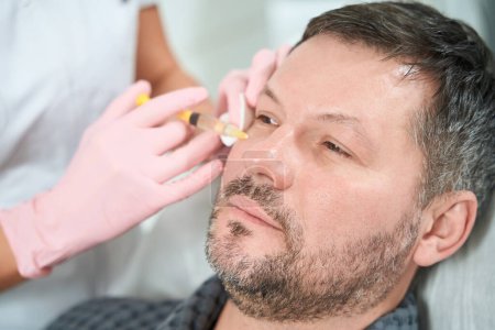 Foto de Hombre sin afeitar recibe inyecciones hipodérmicas en la clínica de medicina estética, médico en guantes de protección - Imagen libre de derechos