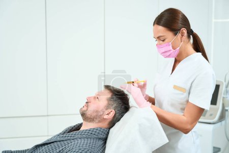 Foto de Cosmetólogo realiza un procedimiento de plasmolifting en el cuero cabelludo, un médico trabaja en una máscara protectora - Imagen libre de derechos