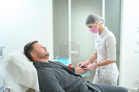 Foto de Una mujer con uniforme médico toma sangre de un paciente, un hombre tiene un torniquete en su brazo - Imagen libre de derechos