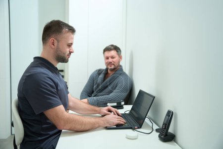 Foto de Nutricionista masculino consulta a un paciente masculino en un centro médico, los hombres están sentados en su escritorio - Imagen libre de derechos