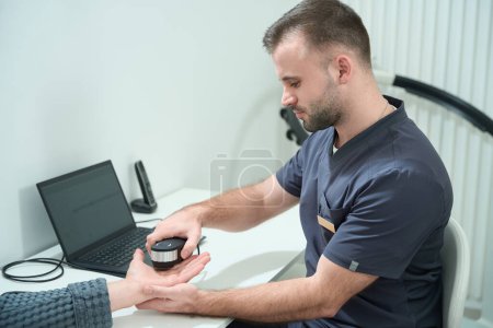 Téléchargez les photos : Spécialiste dans un centre médical effectue une procédure de diagnostic oligoscan, un patient en peignoir - en image libre de droit