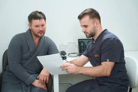 Foto de Paciente de mediana edad en una consulta con un nutricionista en un centro médico, hombres revisando los resultados de las pruebas - Imagen libre de derechos