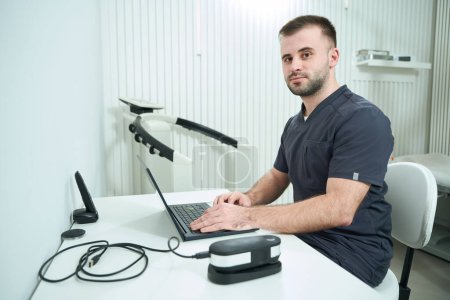 Foto de Nutricionista masculino se sienta en un lugar de trabajo en una computadora portátil, equipo moderno en la oficina - Imagen libre de derechos