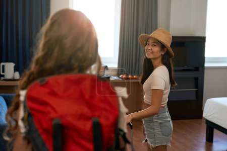 Foto de Mujer sonriente con sombrero de pie en la habitación del hotel, mirando a la cámara - Imagen libre de derechos