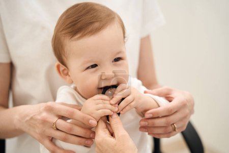 Foto de Pequeño bebé mordisqueando lupa en la mano del oftalmólogo en presencia de la madre - Imagen libre de derechos