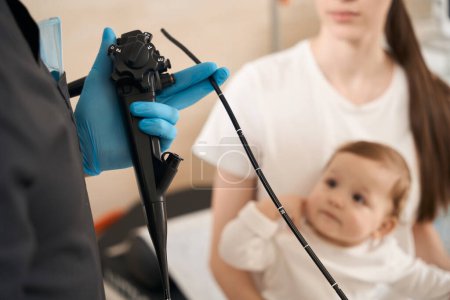 Téléchargez les photos : Photo recadrée d'un médecin tenant un endoscope devant l'enfant et son parent femelle - en image libre de droit