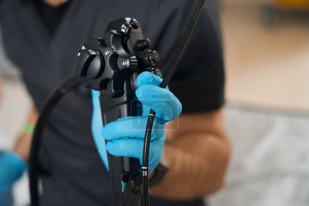 Ausschnittfoto des Endoskopisten, der Endoskop mit behandschuhter Hand vor der Kamera hält