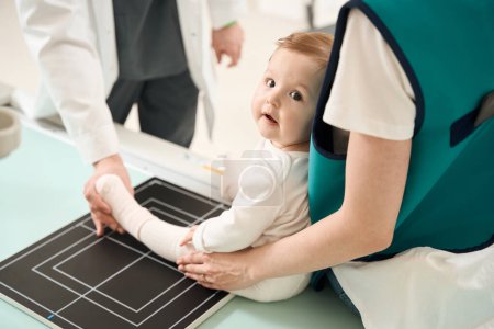 Photo for Cropped photo of radiologic technologist positioning baby leg on radiographic table with help of parent - Royalty Free Image