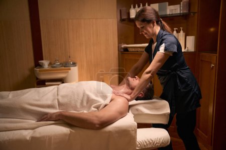 Photo for Smiling masseuse pressing on shoulders of adult man using both hands during massage therapy session - Royalty Free Image